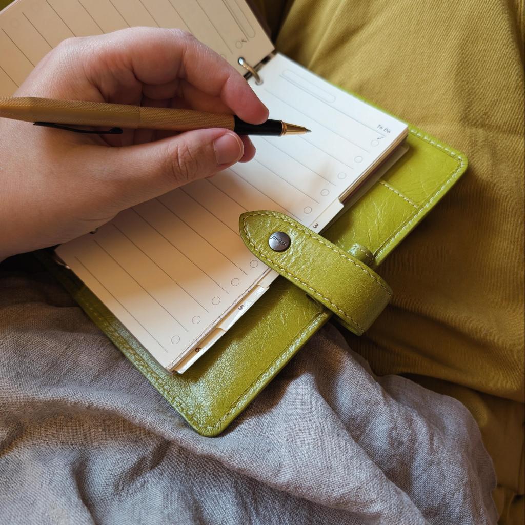 A hand holding a pen above an open notebook with blank pages, resting on a soft, textured surface.